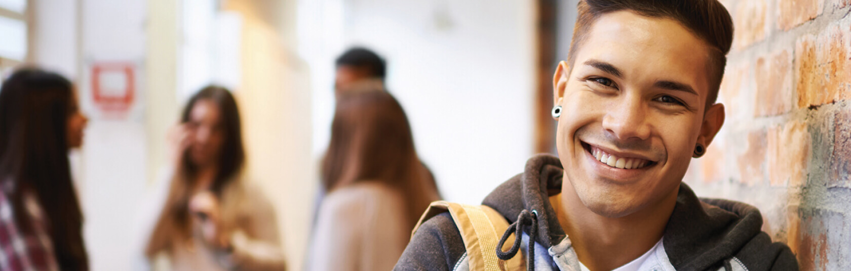 Male student leaning against a wall with a group of other students in the background